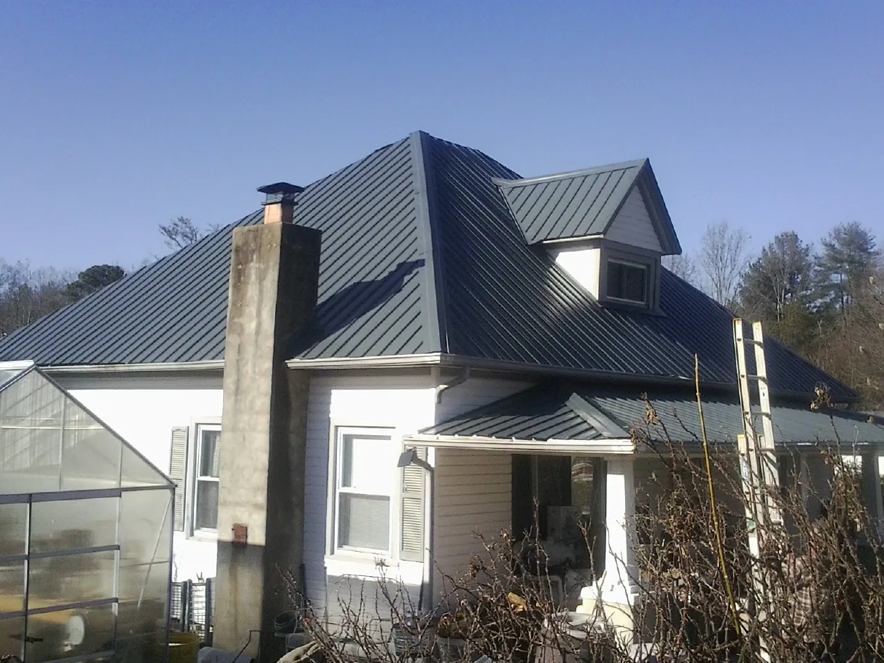Dark blue standing seam metal roof on a white farmhouse with dormer — Slate & Tile Roof Repair by Roofing Brothers in Corona