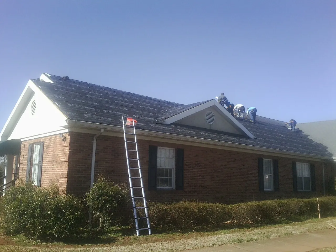 Crew tearing shingles off a brick ranch roof with a ladder set — Emergency Roof Repair work by our crew in Corona