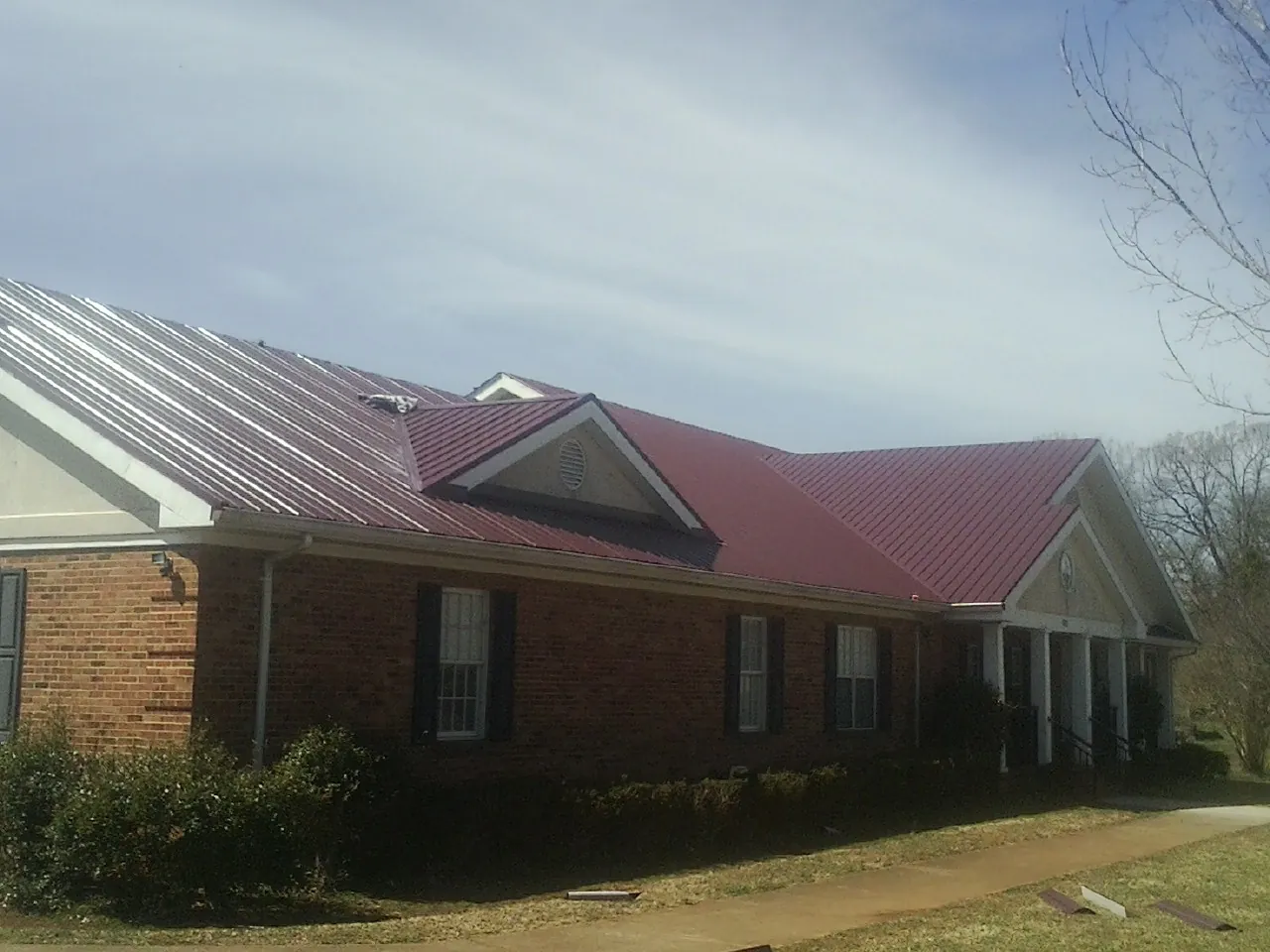 Red metal roof with gabled entries on a long brick building, from a Hail Damage Roof Repair job in Corona