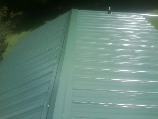 New green metal panels meeting at the ridge of a roof — Flat Roof Repair work by our crew in Corona