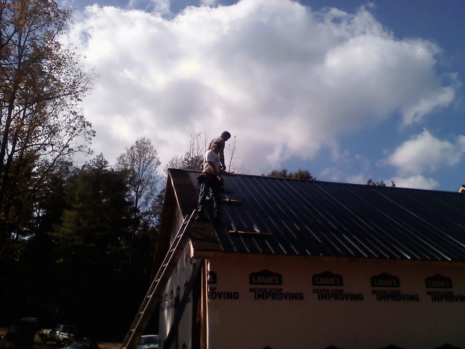 Roofer fastening dark metal panels high against a cloudy sky, from a Roof Inspection job in Corona