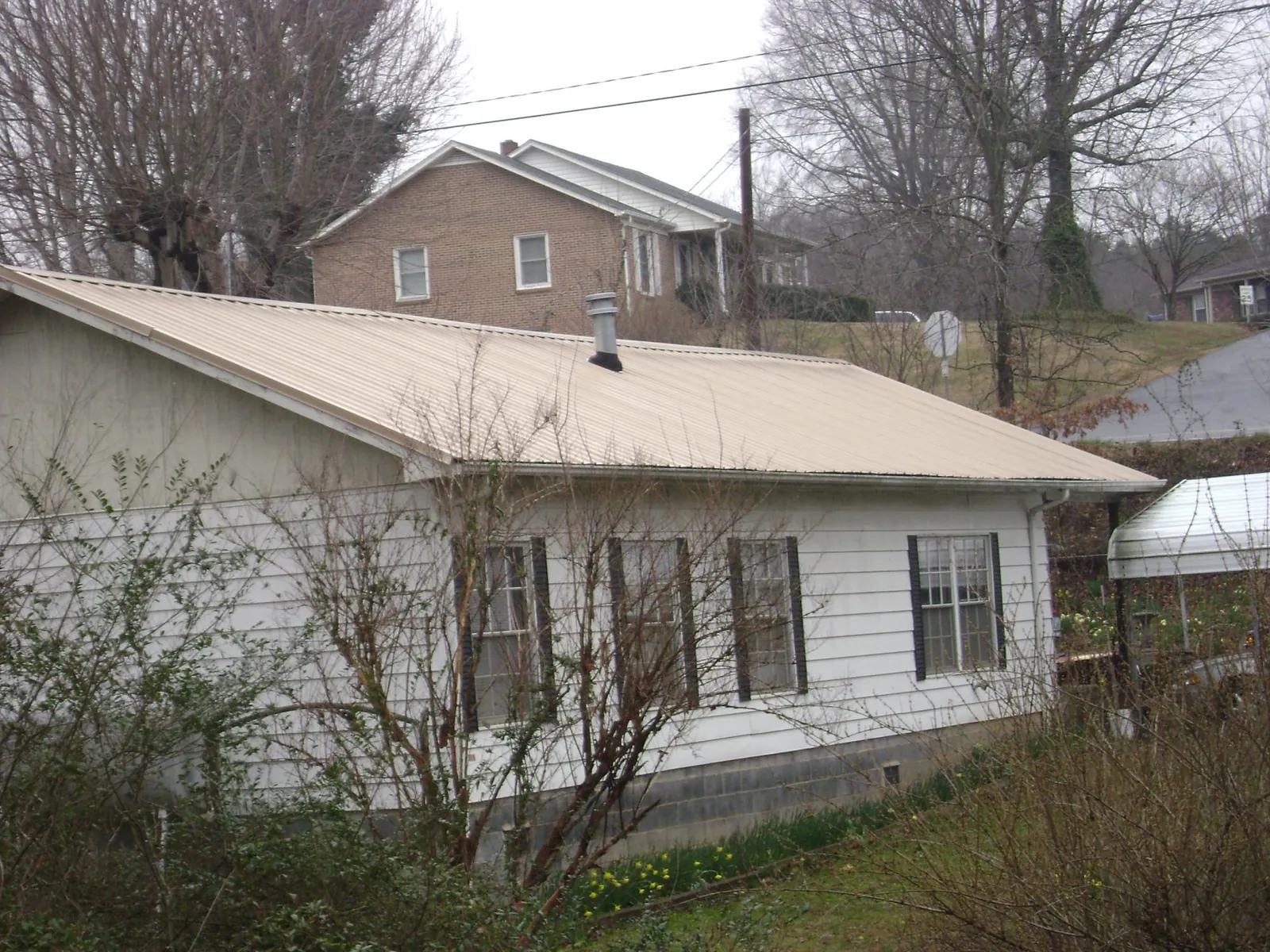 Tan metal roof on a white sided house set into a hillside — Commercial Roofing by Roofing Brothers in Corona