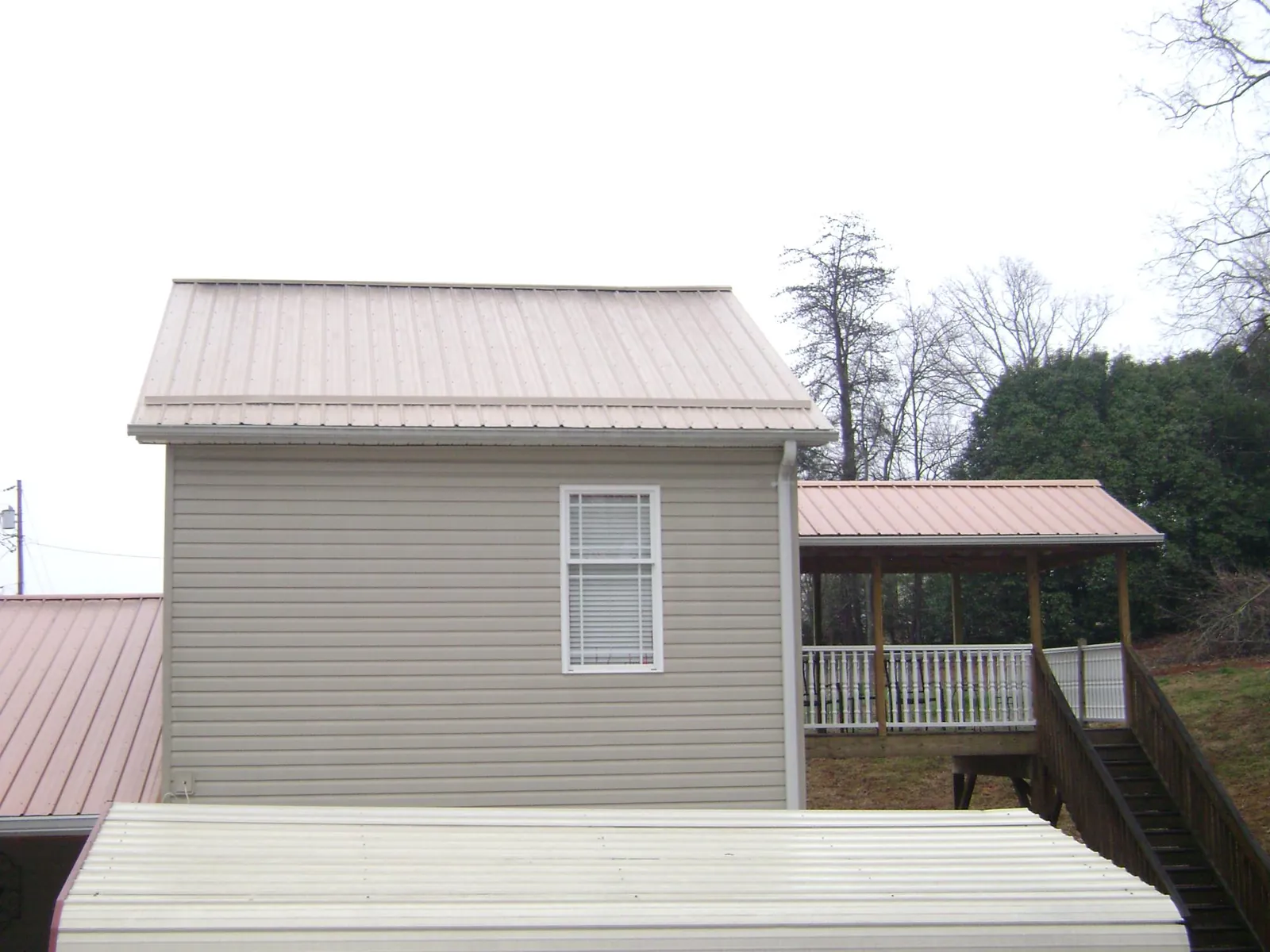 Tan metal roofs on a two story addition and attached porch, from a Roof Replacement job in Corona