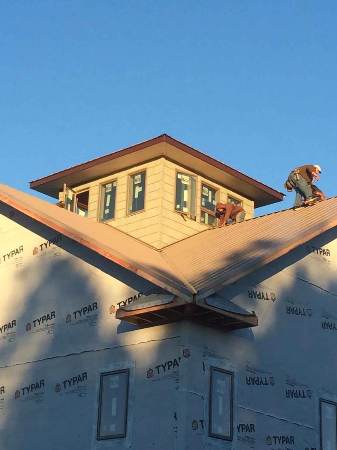 Roofers working around a rooftop cupola on a new metal roof at sunset — Roof Waterproofing in Corona by Roofing Brothers